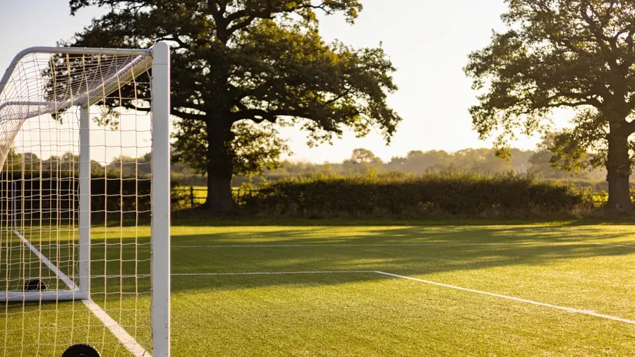 Empty junior football pitch in Surrey on a sunny morning with goalposts and oak trees in the background, children's activities Surrey